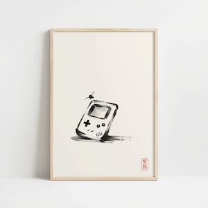 May include: A framed ink wash painting on a light cream background featuring a handheld video game console with a small insect perched on top. The artwork is rendered in black ink with a small red square stamp containing Japanese characters.