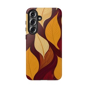 Puede incluir: Una funda de teléfono con un patrón repetido de hojas estilizadas en tonos dorados, amarillos y burdeos. El diseño tiene un aspecto texturizado, con las hojas superpuestas. La funda tiene un módulo de cámara en la parte superior izquierda.