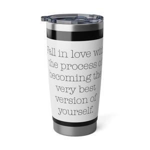 May include: A stainless steel travel tumbler with a black and white design. The tumbler has a black lid and a white body with the text "Fall in love with the process of becoming the very best version of yourself."