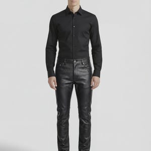 May include: A person wearing a black long-sleeve button-down shirt and black leather pants. The shirt is buttoned up and the pants are fitted. The person is also wearing black shoes. The background is plain white.