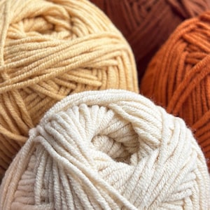 May include: Close-up of several skeins of yarn in cream, yellow, orange, and brown. The yarn is tightly wound, showing the texture of the fibres. Suitable for knitting, crochet, and other yarn crafts.