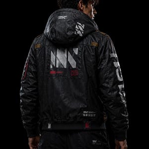 May include: A black hooded jacket featuring white and red graphic prints on the back and sleeves. The back displays large white text and geometric patterns, while the hood and sleeves include additional white branding and orange accents.