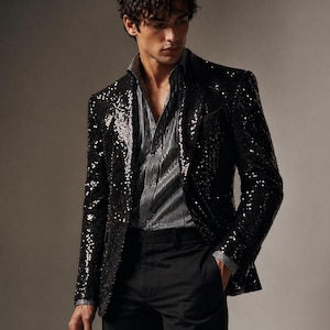 May include: A black sequin blazer with a notched lapel, paired with a striped shirt and black trousers. The blazer's shiny texture contrasts with the matte finish of the pants. The shirt has a silver and black striped pattern.