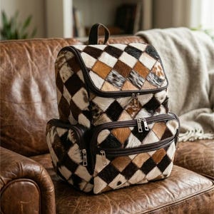 Może przedstawiać: Plecak w stylu patchwork z rombowym wzorem w odcieniach brązu, beżu i kremu. Torba ma górny uchwyt, dwie przegrody zapinane na zamek i regulowane paski. Plecak jest wykonany z teksturowanego materiału.