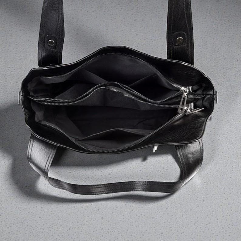 K&ouml;nnte beinhalten: Schwarze Ledertasche mit mehreren Innenf&auml;chern und einem Rei&szlig;verschluss. Die Tasche hat zwei obere Griffe und ein strukturiertes Design. Das Innenfutter ist schwarz.