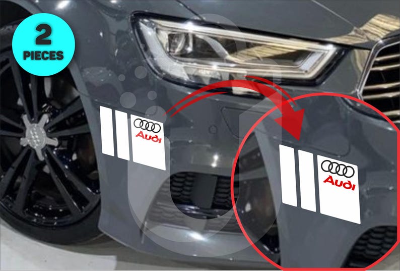 May include: Two-piece set of white and black Audi car decals. The decals feature the Audi logo and three vertical stripes. The image shows the decals applied to a gray car bumper. The text "2 PIECES" is in a blue circle.