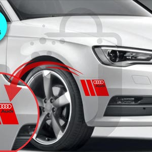 May include: Red and white Audi car decals. The decals feature the Audi logo and three vertical stripes on a red background. The image shows the decals applied to the front of a white car. The text "2 PIECES" is in a blue circle.