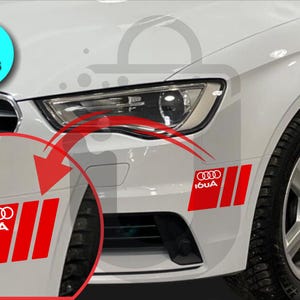 May include: Red and white car decals featuring the Audi logo and three vertical stripes. The decals are shown applied to a white car. The image includes a circular graphic that says "2 PIECES".
