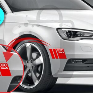 May include: Two-piece set of red and white Audi car decals. Each decal features the Audi logo and three vertical stripes on a red background. The decals are designed to be applied to a car's exterior.