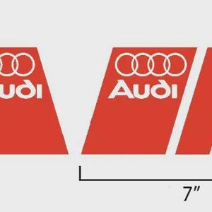 May include: Two red and white Audi decals. Each decal is 7 inches long and 4 inches high. The decals feature the Audi logo and text in white, with three white stripes on a red background.