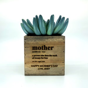 May include: A wooden planter box with a succulent plant. The planter has a definition of the word "mother" engraved on it, along with the text "Happy Mother's Day, Love, Jenny".