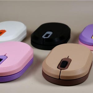 Pode incluir: Cinco ratos de computador coloridos em branco, preto, rosa, bege e roxo. Cada rato tem uma base e uma roda de rolagem de cor contrastante. Os ratos estão dispostos sobre um fundo neutro.