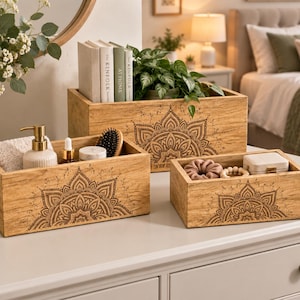 May include: Three rectangular wooden storage boxes featuring a dark brown laser-engraved mandala pattern on the front. The boxes contain various items including books, a small potted plant, a soap dispenser, a hairbrush, and small accessories.
