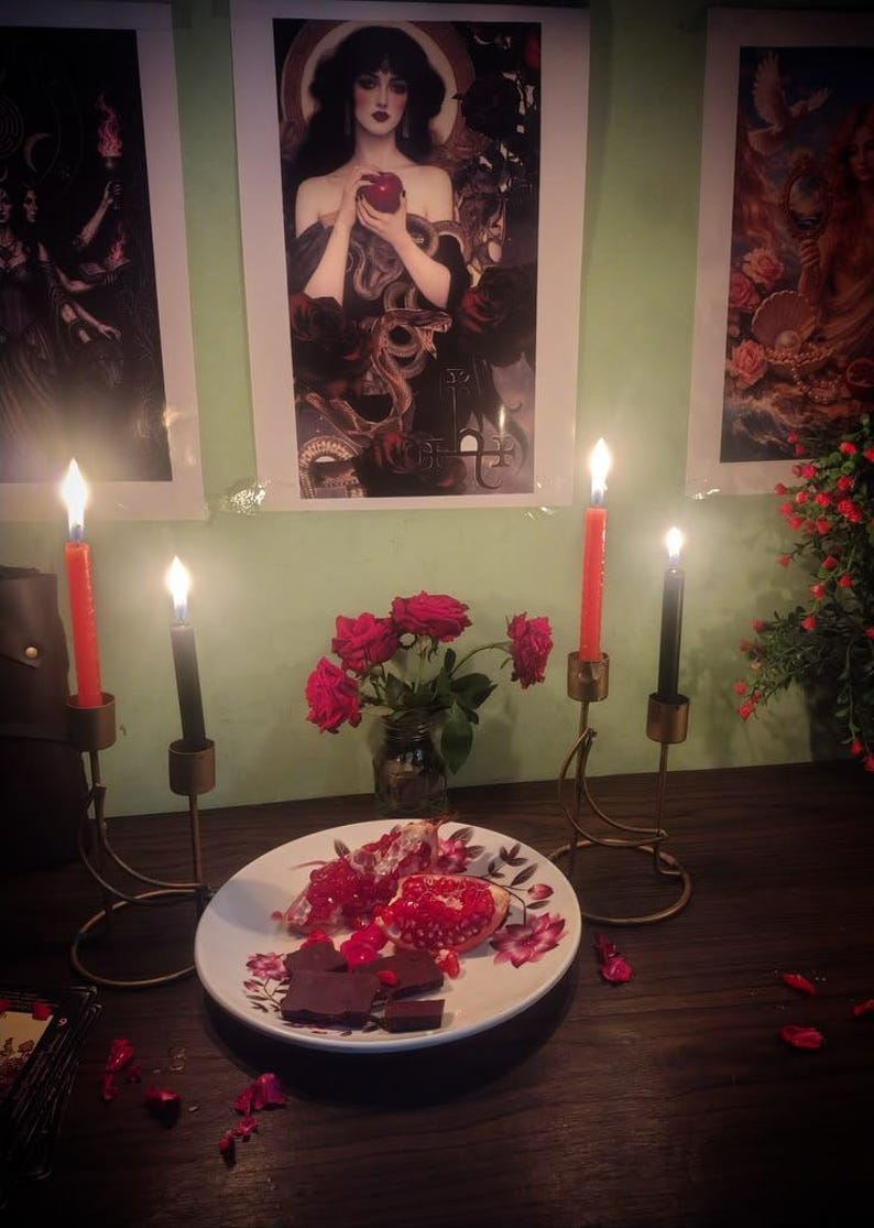 a table with a plate of food, a vase of roses, and three lit candles. The table is set against a green wall with framed artwork.