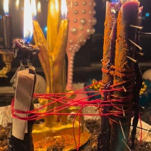 a close-up view of several lit candles, with a pink vase and a potted plant in the background.