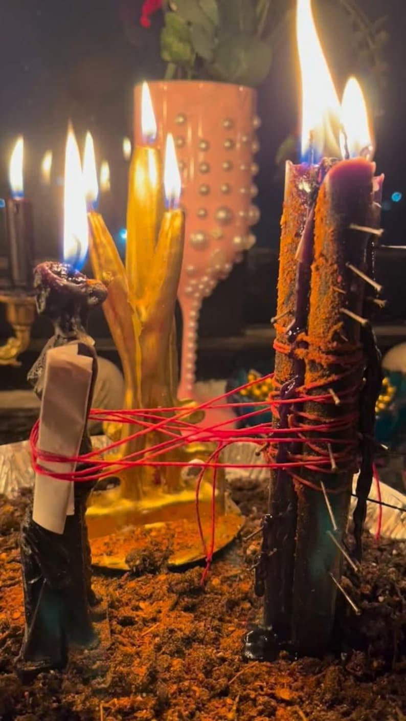 a close-up view of several lit candles, with a pink vase and a potted plant in the background.