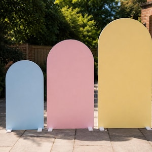 May include: Three freestanding arch-shaped panels of varying heights, arranged in a row. The smallest panel is light blue, the middle panel is pastel pink, and the tallest panel is pale yellow. Each panel features a smooth, solid-coloured surface.