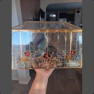 May include: A rectangular glass display box with a gold metal frame featuring arched top panels. The clear glass sides are decorated with painted floral designs in shades of red, blue, yellow, and green, depicting various stems and blossoms.