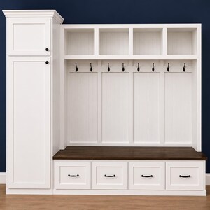 May include: A white wooden entryway storage unit with a tall cabinet, open shelves, hooks, and a bench. The unit has a dark brown bench seat and four drawers with black handles. The background is a dark blue wall.