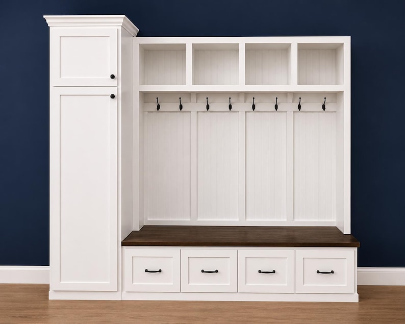 May include: A white wooden entryway storage unit with a tall cabinet, open shelves, hooks, and a bench. The unit has a dark brown bench seat and four drawers with black handles. The background is a dark blue wall.