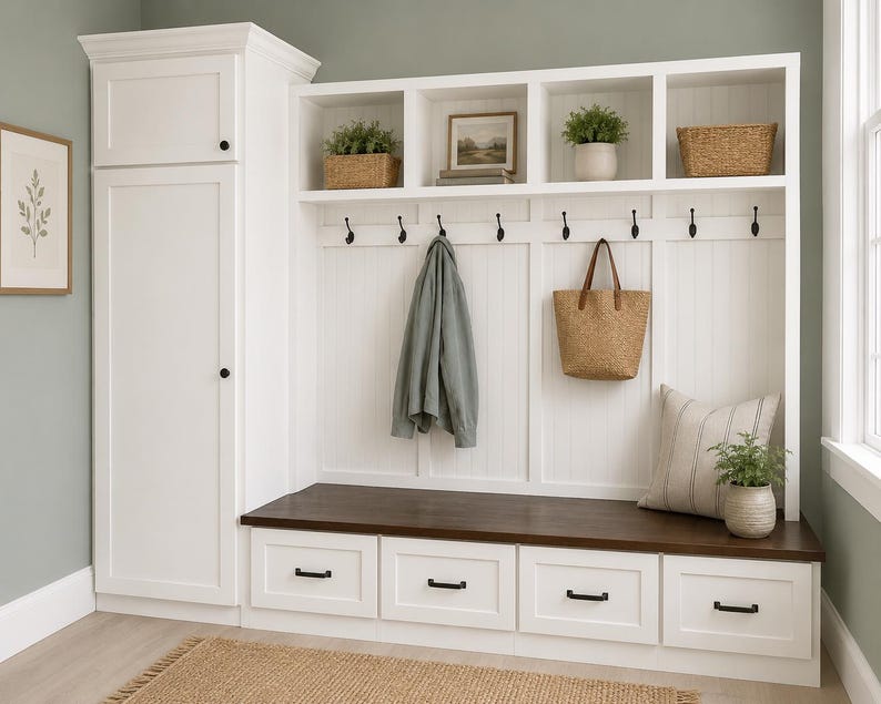 May include: A white entryway storage unit with a dark brown bench and four drawers. Above, there are open shelves with decorative items, hooks for hanging coats, and a woven tote bag. A framed botanical print hangs on the wall.