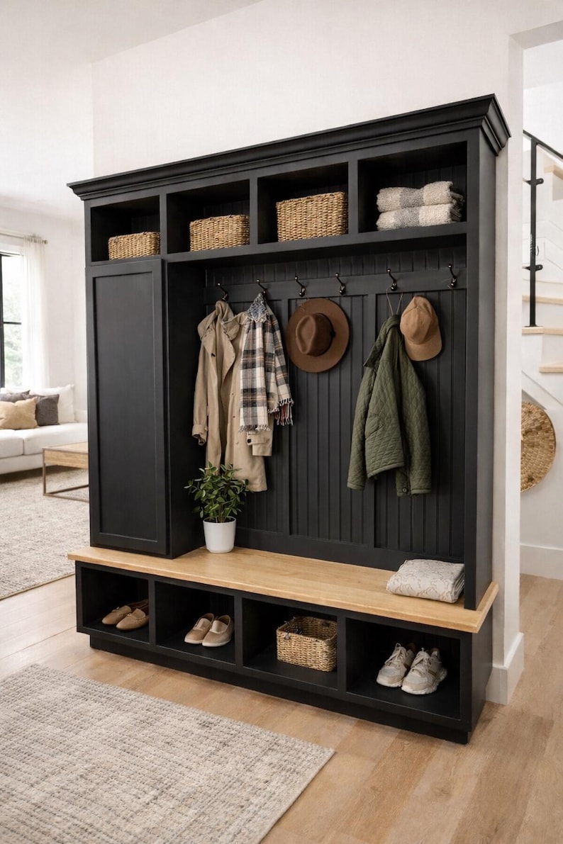 May include: A black entryway storage unit with a bench, shoe cubbies, and upper shelves. Woven baskets and folded blankets are stored on the shelves. Coats, hats, and a scarf hang from hooks. A small potted plant sits on the bench.