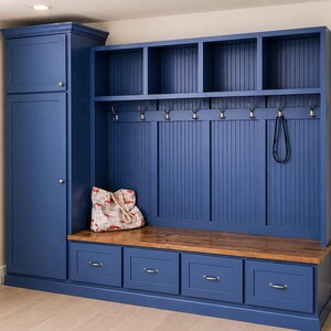 May include: A built-in entryway storage unit in a deep blue color. It features a tall cabinet, open shelves, coat hooks, a bench with drawers, and a wooden top. A decorative bag rests on the bench.