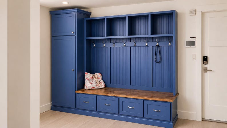 May include: A built-in entryway storage unit in a deep blue color. It features a tall cabinet, open shelves, coat hooks, a bench with drawers, and a wooden top. A decorative bag rests on the bench.
