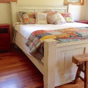 May include: White wooden bed frame with a patchwork quilt and pillows. The bed is in a bedroom with hardwood floors and a red nightstand.