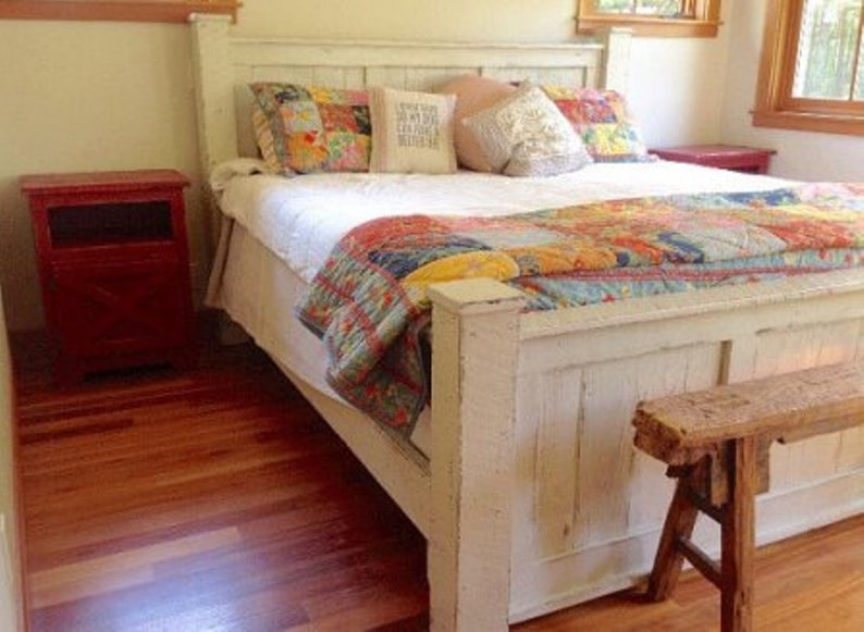 May include: White wooden bed frame with a patchwork quilt and pillows. The bed is in a bedroom with hardwood floors and a red nightstand.