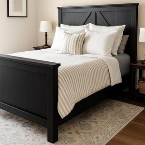 May include: A black wooden bed frame with a matching headboard is the focal point of this bedroom. The bed is made with white pillows and a striped comforter. A patterned rug and two bedside lamps complete the room's decor.