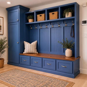 May include: A custom-built, navy blue entryway storage unit with a bench, drawers, and open shelves. Features include brass hardware, woven baskets, and a wooden bench top. A striped pillow and potted plants add decorative touches.