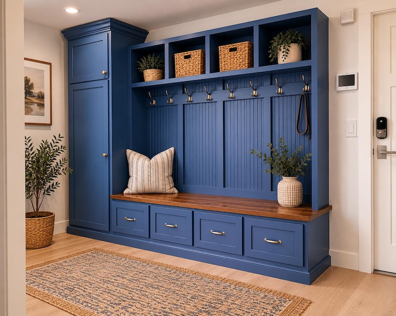 May include: A custom-built, navy blue entryway storage unit with a bench, drawers, and open shelves. Features include brass hardware, woven baskets, and a wooden bench top. A striped pillow and potted plants add decorative touches.