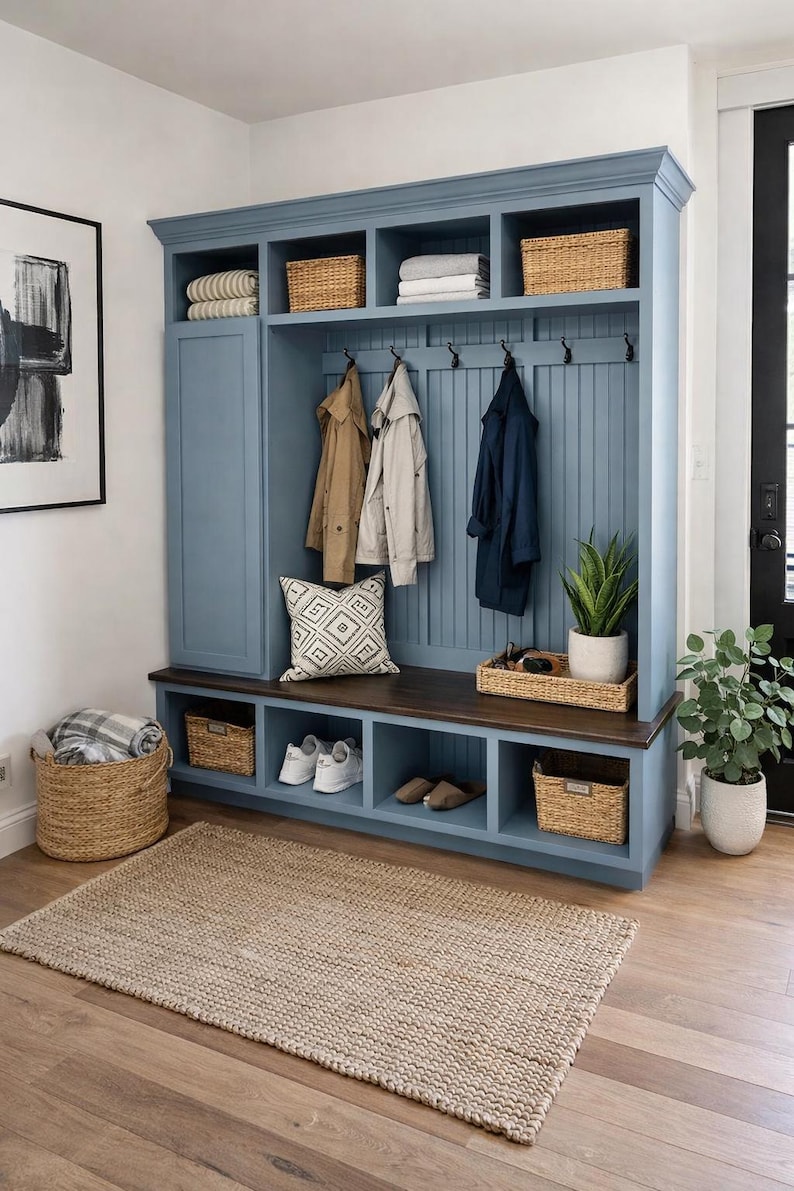 May include: A blue entryway storage unit with a bench, hooks, and cubbies. Wicker baskets, coats, shoes, and a decorative pillow are visible. A woven rug and potted plants complete the space.