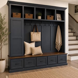 May include: A large dark navy blue mudroom storage unit featuring a tall cabinet, five open upper cubbies with woven baskets, a beadboard back panel with coat hooks, and a wooden bench seat over five drawers with black metal hardware.