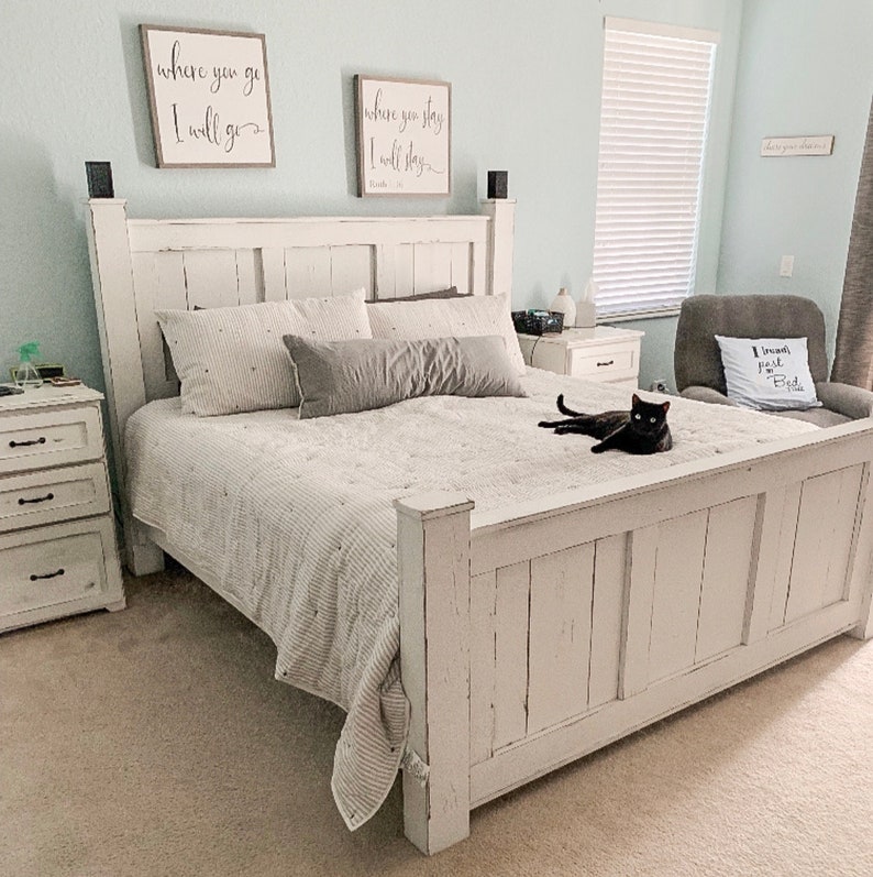 May include: White farmhouse style bed frame with a white and gray striped comforter and a black cat sitting on the bed. The headboard has a distressed white finish and features two signs with the text "where you go I will go" and "where you stay I will stay".