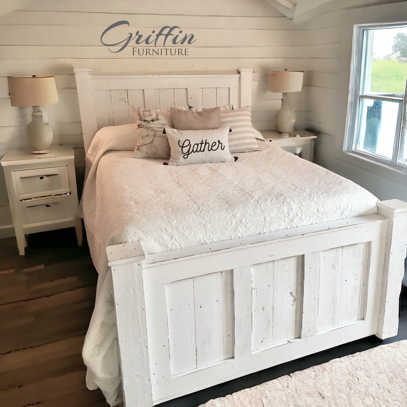 May include: White wooden bed frame with a white headboard and footboard. The headboard has a distressed look and the footboard has a panel design. The bed is made up with white bedding and pillows with the word "Gather" on one of the pillows. The bed is in a bedroom with white walls and a wooden floor.