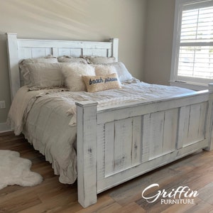 May include: White wooden bed frame with a distressed finish. The headboard has a simple design with vertical planks. The bed is made up with a white and beige bedding set and a pillow with the text "beach please".