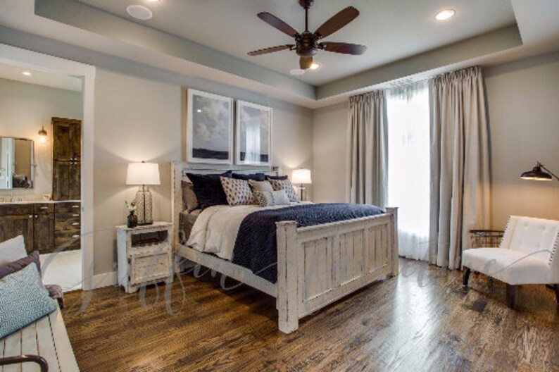 May include: A whitewashed wood bed frame with a white, blue, and gray patterned comforter. The bed is in a bedroom with white walls, wood floors, and a large window with white curtains.
