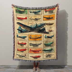 May include: A beige throw blanket featuring a vintage airplane design. The blanket showcases various aircraft illustrations in a grid pattern, with a large blue plane as the central focus. The edges have a fringed trim.