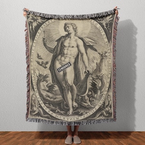 May include: A woven throw blanket featuring a classical illustration of a nude male figure holding a torch and a lyre, surrounded by mythical creatures and text. The artwork is in black and white with a fringed edge.