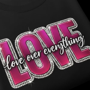 May include: Black sweatshirt with a large, sparkling pink "LOVE" graphic. The word "LOVE" is outlined with rhinestones and has the phrase "over everything" in a cursive font.