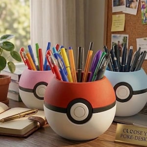 May include: Three spherical desk organizers shaped like Poké Balls in red, pink, and blue, each featuring a central white button and black band. These containers hold various colorful pens and markers, providing a functional storage solution.