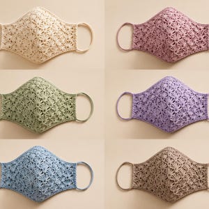 Op de afbeelding: Zes gezichtsmaskers met een gedetailleerd gehaakt schelppatroon. De maskers zijn verkrijgbaar in crème, oudroze, saliegroen, lavendel, lichtblauw en bruin. Elk masker is voorzien van bijpassende elastische oorlussen en een puntige naad.