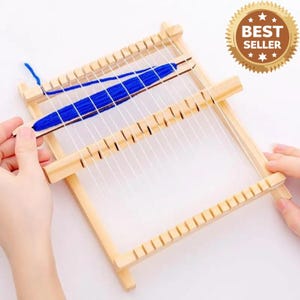 May include: A small, rectangular wooden weaving loom with white warp threads and blue yarn. The loom has a series of notches along the top and bottom edges. A wooden shuttle holds the blue yarn. The image includes a "BEST SELLER" sticker.