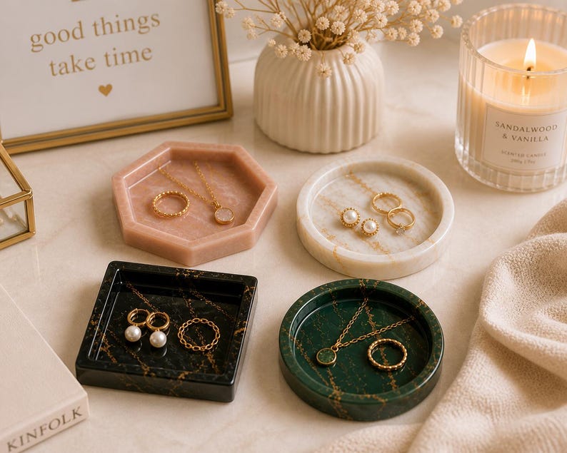 May include: A collection of jewelry trays in various shapes and colors, including pink, white, black, and green, each holding rings and necklaces. A lit candle and a framed print with the text "good things take time" are also present.