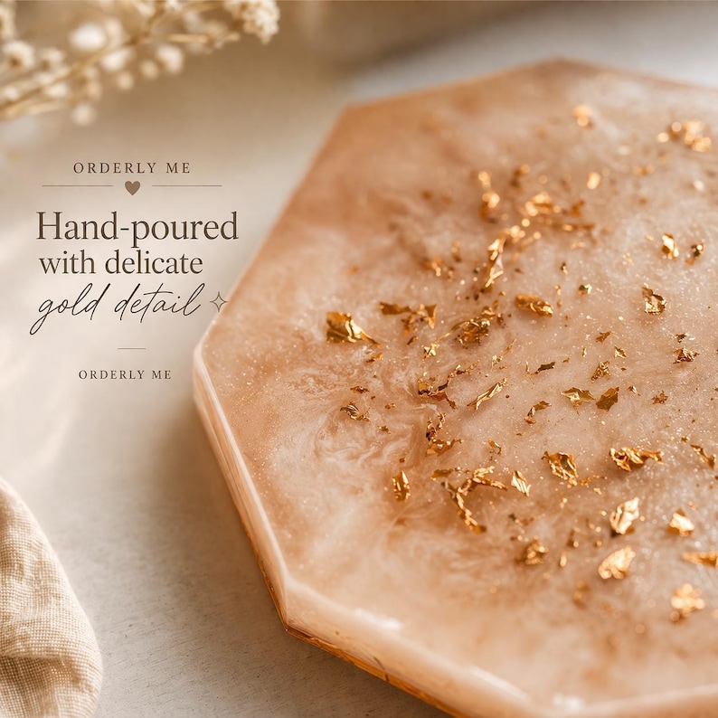 May include: A hexagonal, hand-poured coaster with a pearlescent, light peach hue. The coaster is adorned with delicate gold leaf details. The text "ORDERLY ME" and "Hand-poured with delicate gold detail" are visible.