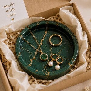 May include: A gift box containing a green marble-patterned jewelry tray with gold accents. The tray holds a gold necklace, ring, and earrings with pearl drops. A small card reads "made with care."