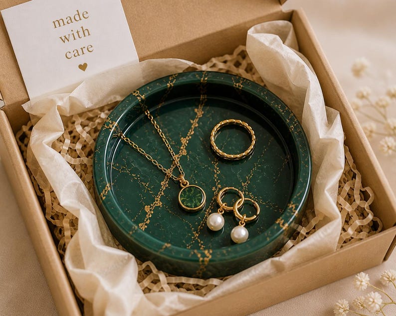 May include: A gift box containing a green marble-patterned jewelry tray with gold accents. The tray holds a gold necklace, ring, and earrings with pearl drops. A small card reads "made with care."