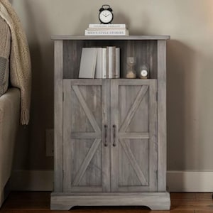 May include: A gray wooden cabinet with a rustic design. The cabinet has two doors with a diagonal cross pattern and metal handles. The top shelf holds books, a small clock, and a decorative hourglass. The cabinet is a piece of furniture.